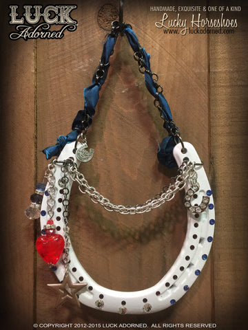 AMERICAN STYLE is a glossy white lucky horseshoe, hung by a gunmetal chain with a shimmery, blue ribbon through it.